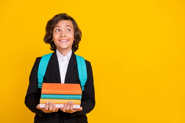 Photo of dreamer schoolboy hold stack book look empty space wear bag black uniform isolated yellow color background — Fotografia de Stock
