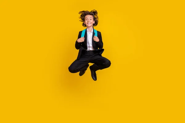 Zdjęcie śmieszne beztroski mały chłopiec skok cieszyć się przerwy nosić torbę czarny mundur odizolowany żółty kolor tło — Zdjęcie stockowe
