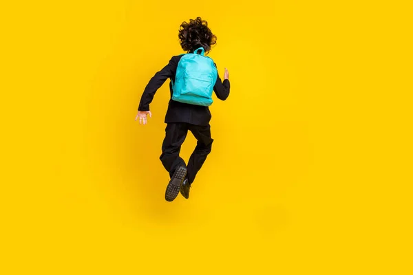 Rückseite Foto von aktiven Schüler laufen Sprung tragen Rucksack schwarze Uniform isoliert gelbe Farbe Hintergrund — Stockfoto