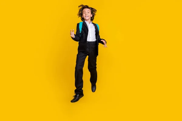 Photo of funky inspired joyful schoolboy jump wear backpack black uniform isolated yellow color background — Stok fotoğraf