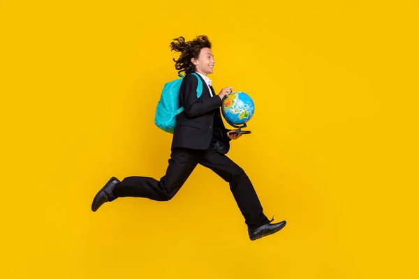 Profil fotografie sportovního malého chlapce skok běh držet glóbus nosit batoh černá uniforma izolované žlutá barva pozadí — Stock fotografie