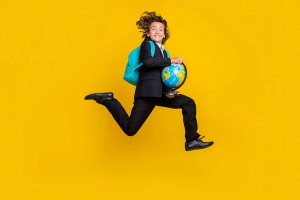 Photo of energetic little boy jump rush run hold globe wear rucksack black uniform isolated yellow color background — Foto Stock