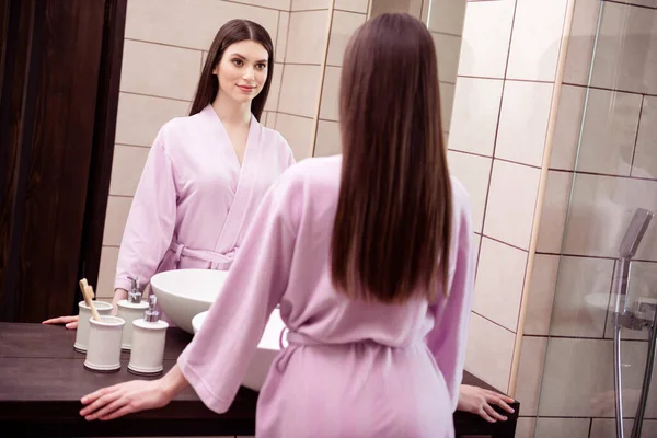 Foto af charmerende sød ung kvinde lyserød natbeklædning ser spejl smilende indendørs hjem værelse - Stock-foto