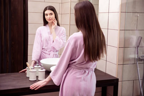 Foto af funky yndig ung dame lyserød badekåbe sleepwear søger spejl arm kind kindben indendørs værelse hjem - Stock-foto