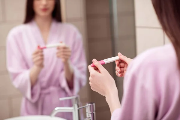 Foto af ung kvinde holder graviditetstest positiv barsel forventer barn slid pyjamas badeværelse indendørs - Stock-foto