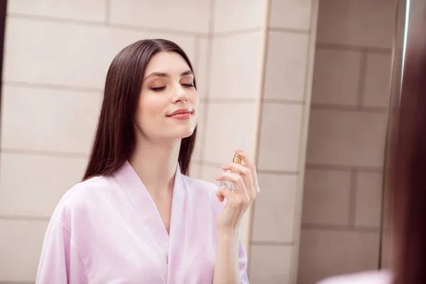 Foto af ung attraktiv kvinde glad positivt smil nyde spray ny frisk parfume aroma morgen badekåbe indendørs - Stock-foto