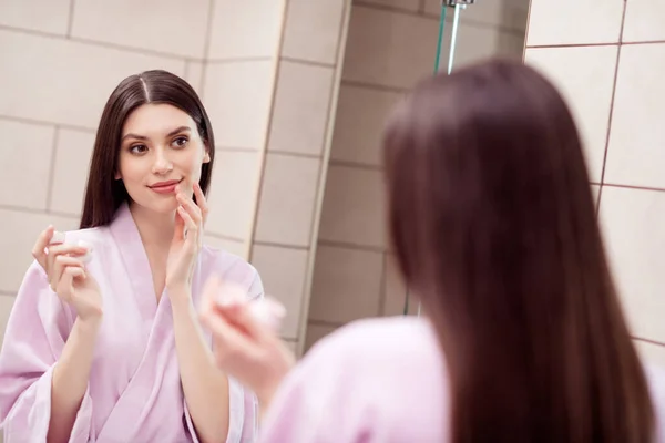 Foto de adorável mulher bonita camisola rosa roupão de banho espelho aplicando bálsamo labial dentro de casa casa quarto — Fotografia de Stock