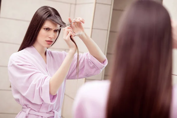 Foto af ung attraktiv pige ulykkelig trist vred klippe hendes hår beskadiget ny frisure bære badekåbe indendørs - Stock-foto