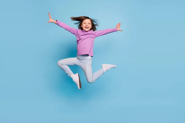Fénykép aranyos vicces kis iskoláslány öltözött lila garbó mosolygós ugrás magas elszigetelt kék háttér — Stock Fotó