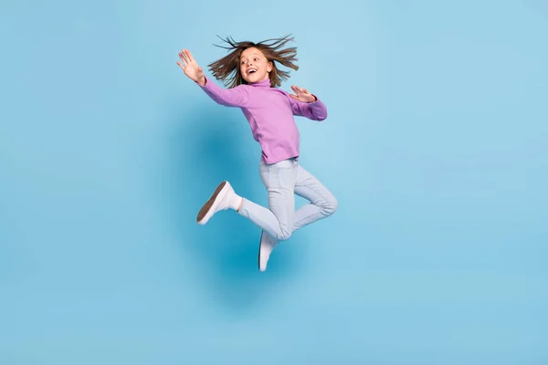 Foto de divertida adorable colegiala pequeña vestida de cuello alto violeta sonriente saltando alto aislado color azul fondo —  Fotos de Stock