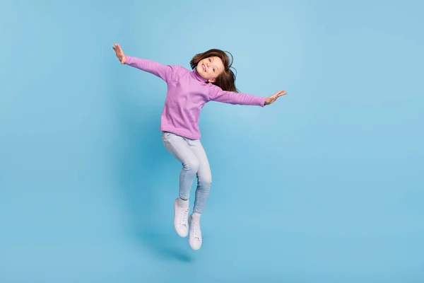 Photo of pretty charming school girl wear purple turtleneck jumping high smiling isolated blue color background