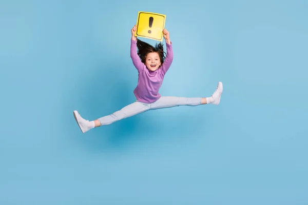 Фото очаровательной милой школьницы носить фиолетовый водолазка прыжки высоко держа карточку внимания улыбаясь изолированный синий цвет фона — стоковое фото