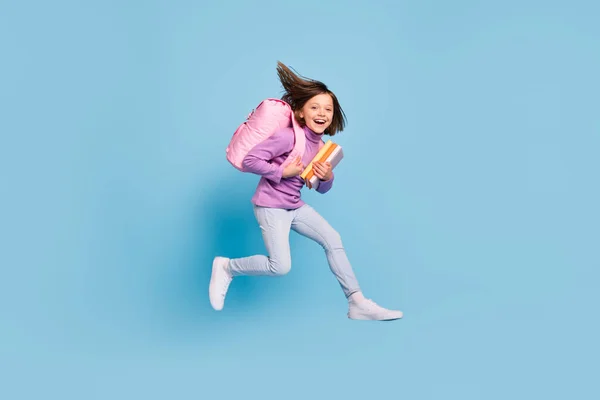 Full length body size photo small girl jumping up running to school with books isolated pastel blue color background