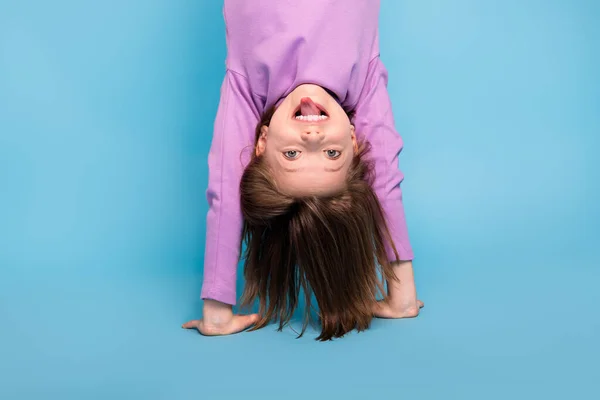 Foto van grappige gek schoolmeisje dragen paarse coltrui staande armen tonen tong glimlachen geïsoleerde blauwe kleur achtergrond — Stockfoto