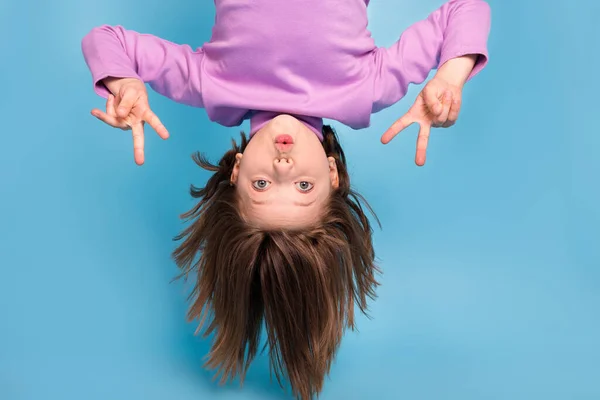 Foto van grappig schattig klein schoolmeisje gekleed violet coltrui vliegen ondersteboven tonen v-tekens geïsoleerde blauwe kleur achtergrond — Stockfoto