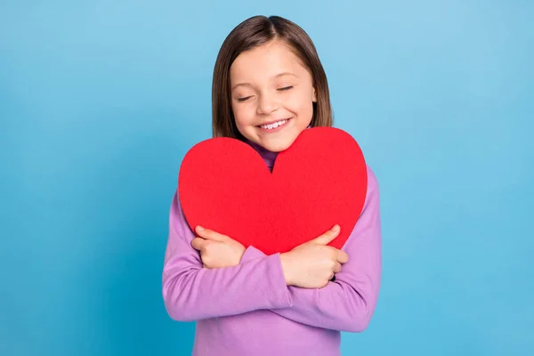 Foto de engraçado encantador pequena estudante vestida gola alta violeta abraçando vermelho coração fechado olhos isolado azul cor de fundo — Fotografia de Stock