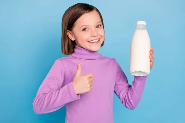 Fotoğraftaki küçük kız gülümsüyor. Sütlü şişeyi tutuyor. Baş parmağını kaldırıyor. — Stok fotoğraf
