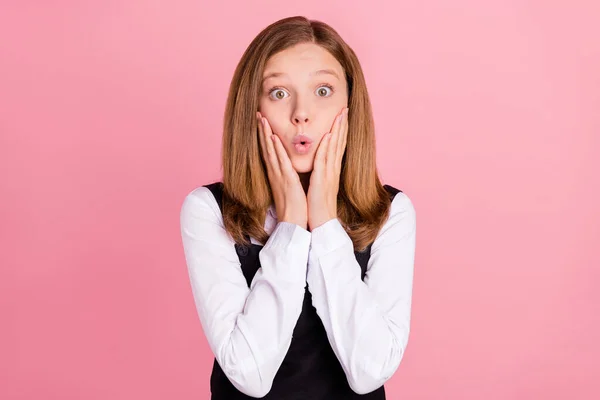 Photo of shocked funny school girl wear white black uniform arms cheeks big eyes isolated pink color background