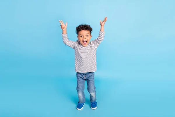 Вид полного размера тела симпатичного веселого изумленного мальчика, поднимающего руки вверх на ярко-голубом фоне — стоковое фото