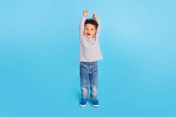 Повнометражний вигляд на тіло гарного веселого хлопчика, що піднімається руками вгору, святкуючи ізольований на яскраво-блакитному фоні — стокове фото