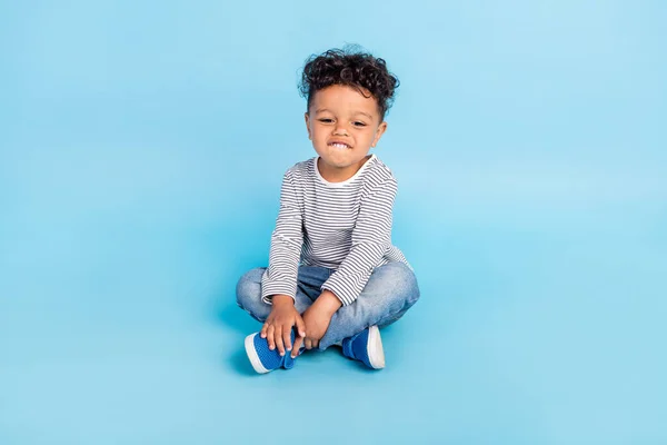 Портрет привлекательного жизнерадостного мальчика, сидящего на полу на ярко-голубом фоне — стоковое фото