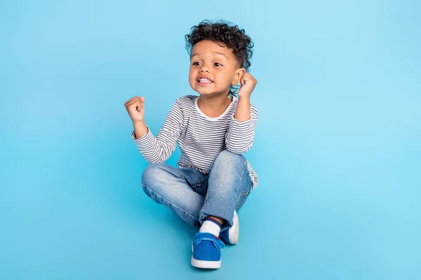 Retrato de niño alegre atractivo sentado en el suelo celebrando suerte aislado sobre fondo de color azul brillante — Foto de Stock
