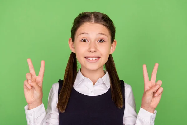 Foto de la encantadora chica de la escuela brillante vestida con ropa formal sonriendo mostrando signos v aislados de color verde de fondo — Foto de Stock