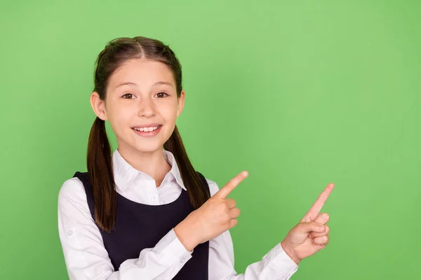 Foto de menina da escola feliz sorriso positivo indicar dedos espaço vazio anúncio aconselhar promo isolado sobre fundo cor verde — Fotografia de Stock