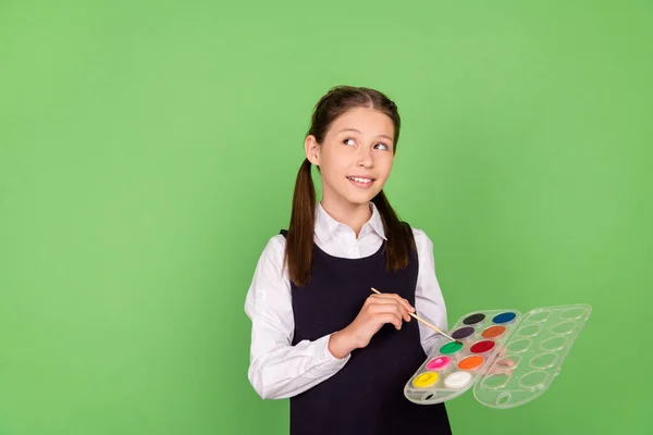 Фотопортретна школярка, що тримає кольорову палітру з пензлем, виглядає як копія, ізольований пастельний зелений кольоровий фон — стокове фото