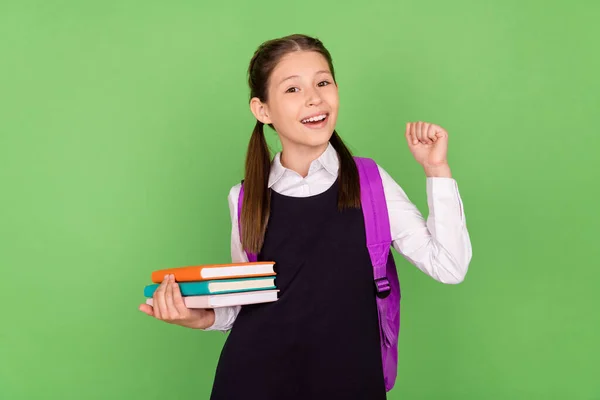 Foto porträtt skolflicka med ryggsäck bok högen gest som vinnare isolerad pastell grön färg bakgrund — Stockfoto