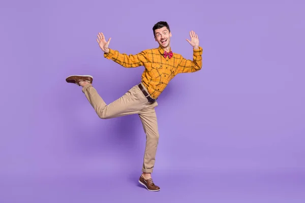 Foto de divertido lindo joven vestido camisa a cuadros bailando de pie una pierna aislado color púrpura fondo — Foto de Stock