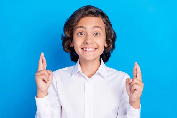 Foto de dulce encantador niño de la escuela usar traje formal sonriendo dedos cruzados aislado color azul fondo —  Fotos de Stock