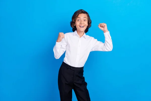 Photo of charming lucky school boy wear formal outfit smiling rising fists isolated blue color background — Stock Photo, Image