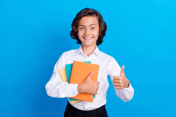 Foto di adorabile grazioso scolaro indossare abiti formali abbracciare libro mostrando pollice in su sorridente isolato sfondo di colore blu — Foto Stock