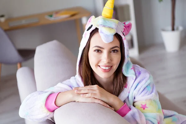 Foto de chica adorable sincera mirada cámara toothy radiante sonrisa relajarse sentarse sofá usar cosplay unicornio kigurumi en el interior —  Fotos de Stock