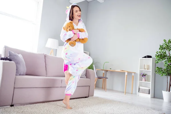 Foto de sonho adorável adorável bonito funky senhora dança relaxar abraçar brinquedo urso desgaste unicórnio cosplay kigurumi dentro de casa — Fotografia de Stock