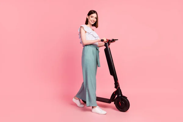 Volledige lengte profiel zijkant foto van jong meisje gelukkig positief glimlach gaan lopen houden elektrische fiets geïsoleerd over roze kleur achtergrond — Stockfoto