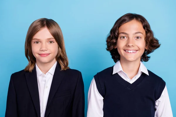 Фотопортрет двух одноклассников, улыбающихся в униформе, сидящих на изолированном пастельно-голубом фоне — стоковое фото