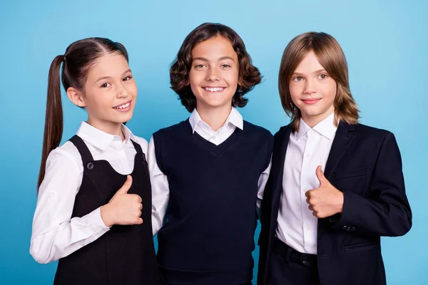 Foto de engraçado brilhante crianças em idade escolar usar uniforme abraço abraçando mostrando polegares para cima sorrindo isolado azul cor de fundo — Fotografia de Stock