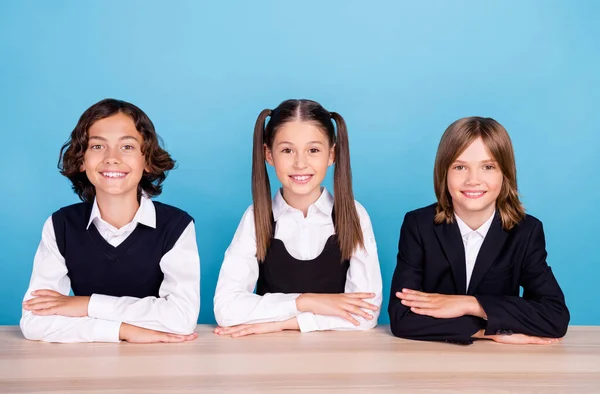 Fotografie okouzlující sladké školáci formalwear usměvavý sedací stůl paže složené poslech lekce izolované modré barvy pozadí — Stock fotografie