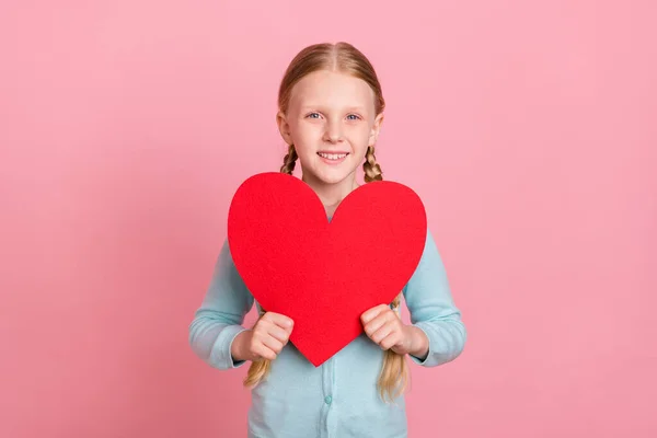 Foto de menina da escola muito brilhante desgaste azul casaco de lã segurando grande coração vermelho sorrindo isolado cor de fundo rosa — Fotografia de Stock