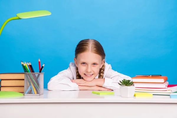 Foto portret schoolmeisje zitten aan bureau in de buurt van boek stapel glimlachen geïsoleerde pastel blauwe kleur achtergrond — Stockfoto