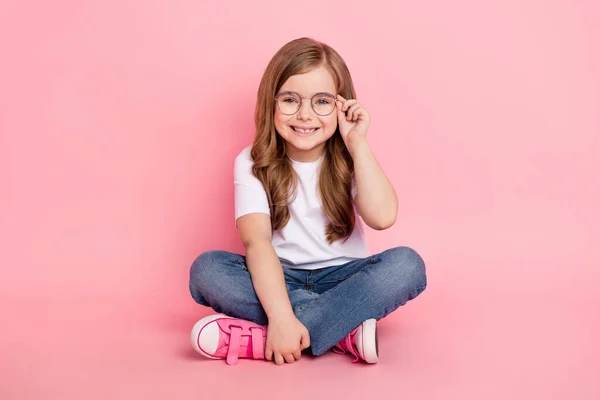 Fotografie snu legrační holčička sedět podlaha nosit brýle bílá tričko džíny boty izolované růžové barvy pozadí — Stock fotografie
