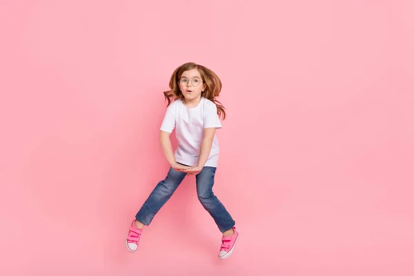 Fotografie šokované legrační dívka skok omg reakce nosit brýle bílá tričko džíny izolované růžové barvy pozadí — Stock fotografie