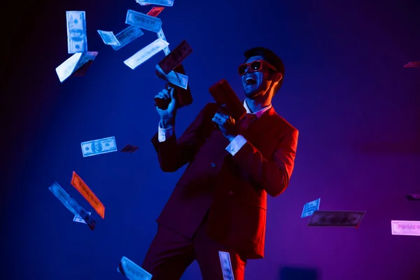 Photo of funky charming young man wear glamour costume eyewear dancing shooting money gun isolated dark blue color background — Stock Photo, Image