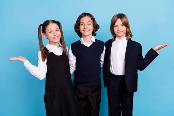 Photo portrait school mates smiling in uniform keeping empty space on palms isolated pastel blue color background — Stock Photo, Image