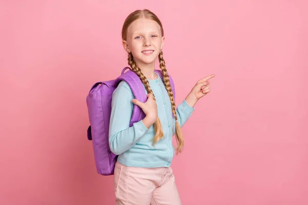 Foto di eccitato carino studentessa vestito blu cardigan sorridente zaino indicando dito vuoto spazio isolato colore rosa sfondo — Foto Stock