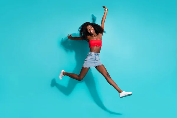 Plná velikost fotografie bláznivé šťastný afro americká mladá žena vyskočit úsměv izolované na pastelové modré barvy pozadí — Stock fotografie