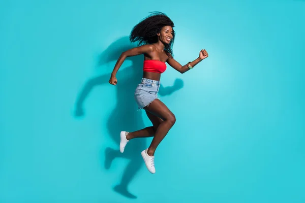 Foto de corpo inteiro de morena afro-americana jovem saltar para cima correr espaço vazio isolado no fundo de cor azul — Fotografia de Stock
