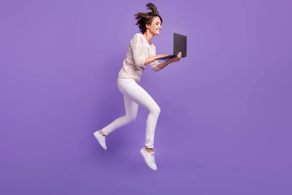 Full längd foto av ganska roligt ung kvinna bära stickad skjorta hoppa hög skriva modern gadget isolerad violett färg bakgrund — Stockfoto